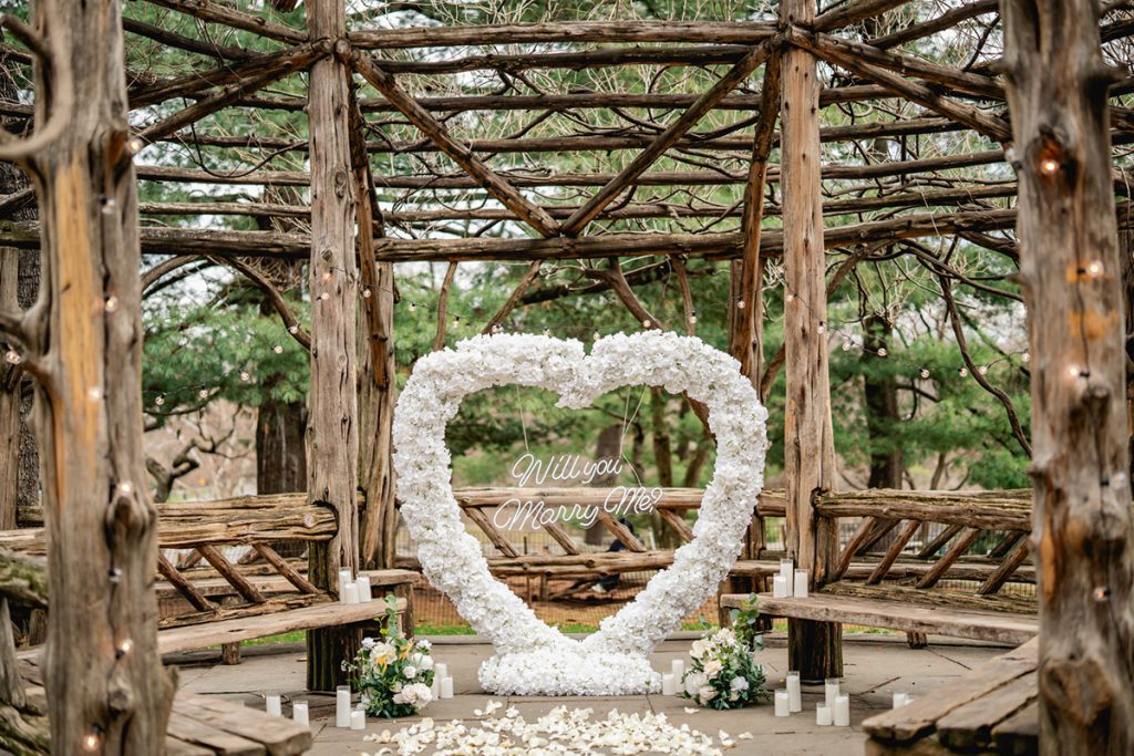 White flower heart with a Will You Marry Me sign set up inside the Cop Cot gazebo in Central Park