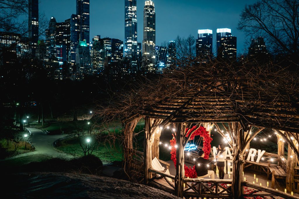 Secret Central Park gazebo lit up at night with a red heart and MARRY ME letters, the Midtown skyline behind