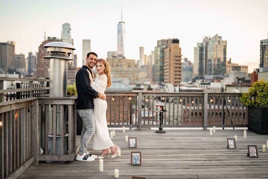 Couple on a wooden rooftop deck lined with candles and framed photographs, the downtown skyline behind them