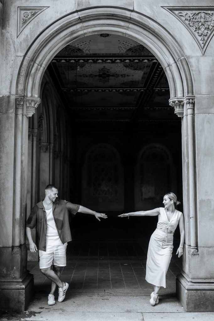 Black and white photograph of an engaged couple in a stone arcade beside St. Patrick's Cathedral, New York