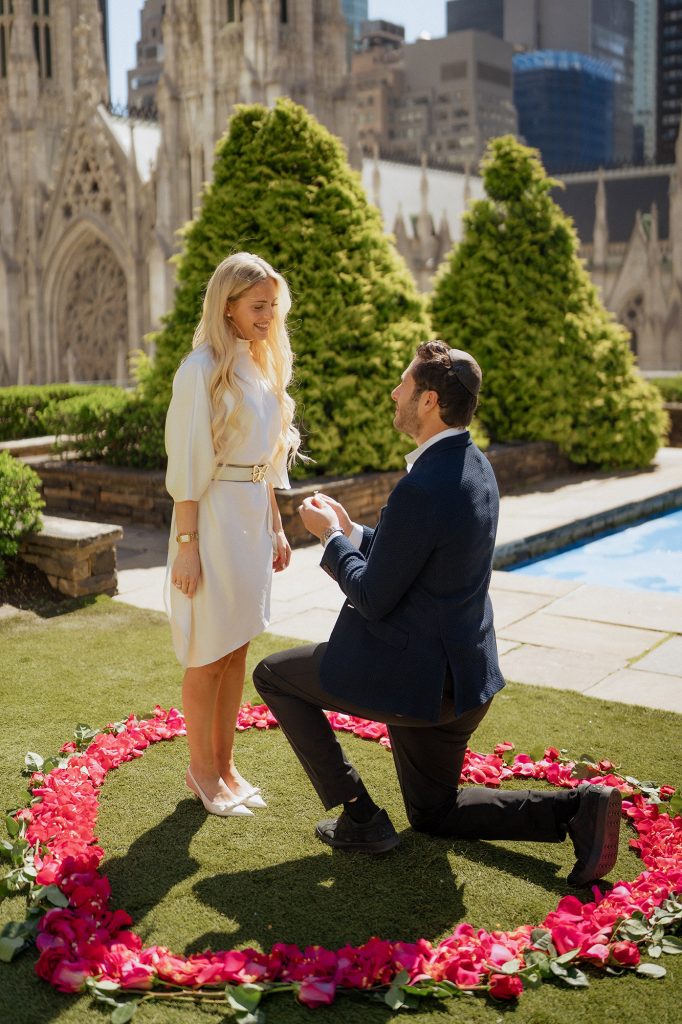 Man proposing inside a heart of pink petals at 620 Loft & Garden, St. Patrick's Cathedral behind