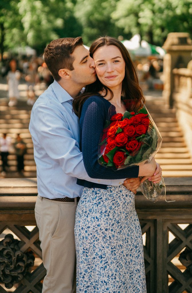 Newly engaged couple with red roses at Bethesda Terrace in Central Park after a surprise proposal