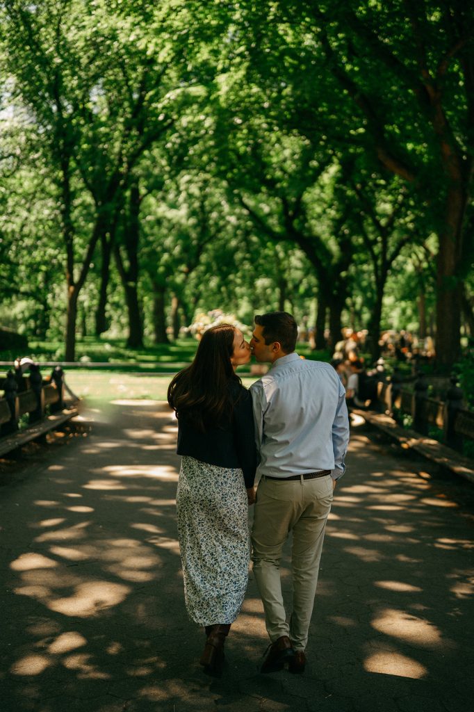 Newly engaged couple walking away hand in hand down The Mall in Central Park under the elms