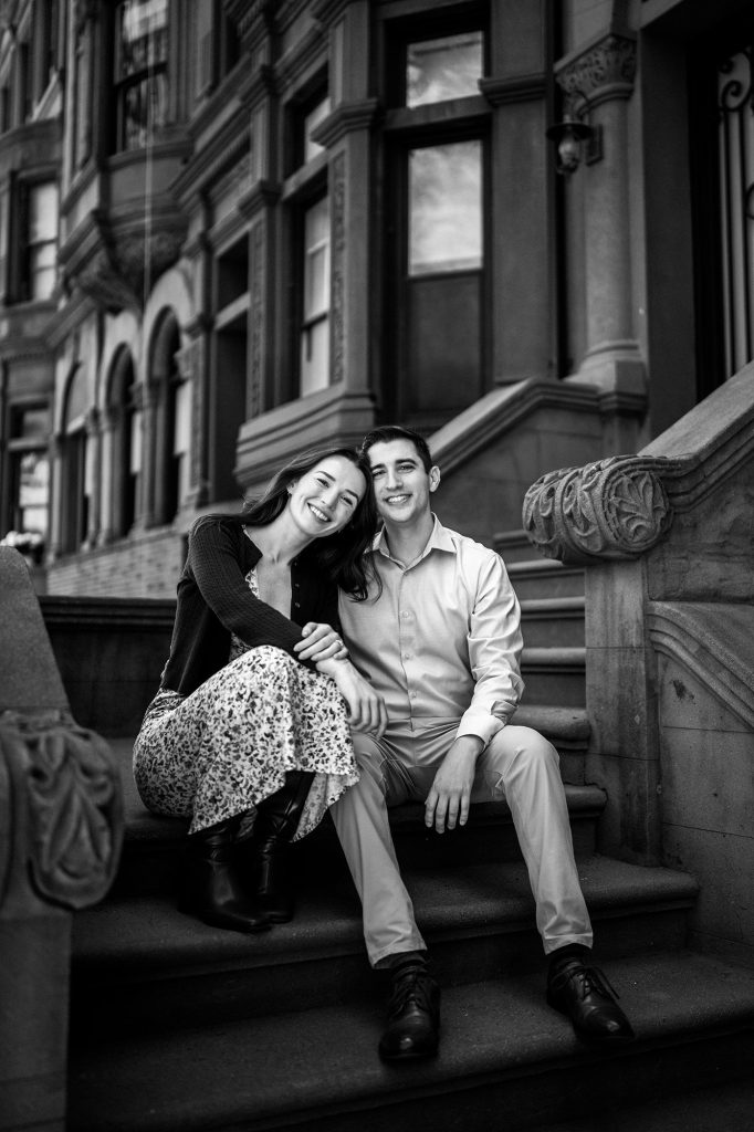 Black and white portrait of an engaged couple sitting on a New York brownstone stoop