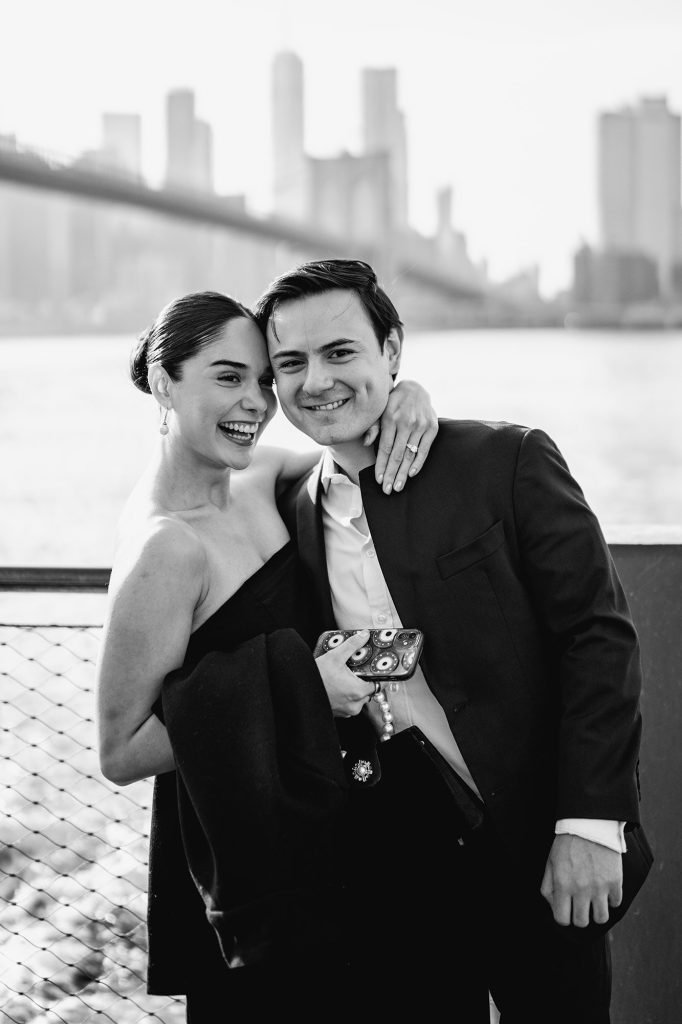 Black and white engagement portrait in DUMBO, Brooklyn, with the Manhattan skyline behind