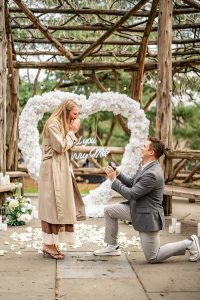 Surprise proposal under a white floral heart at Cop Cot, the rustic pergola in Central Park