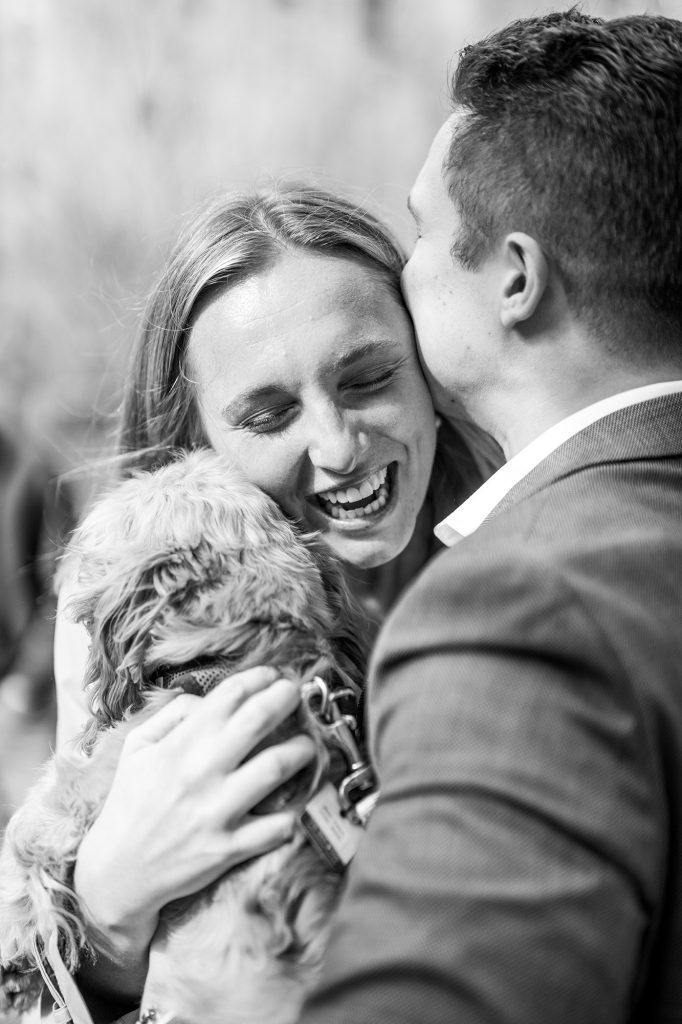 Black and white photograph of a newly engaged couple laughing with their dog in Central Park
