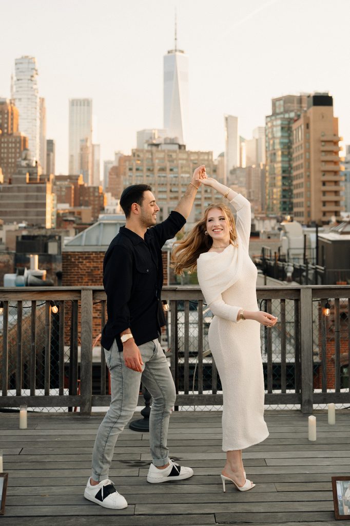 Man spinning his fiancee on a Manhattan rooftop with One World Trade Center behind them