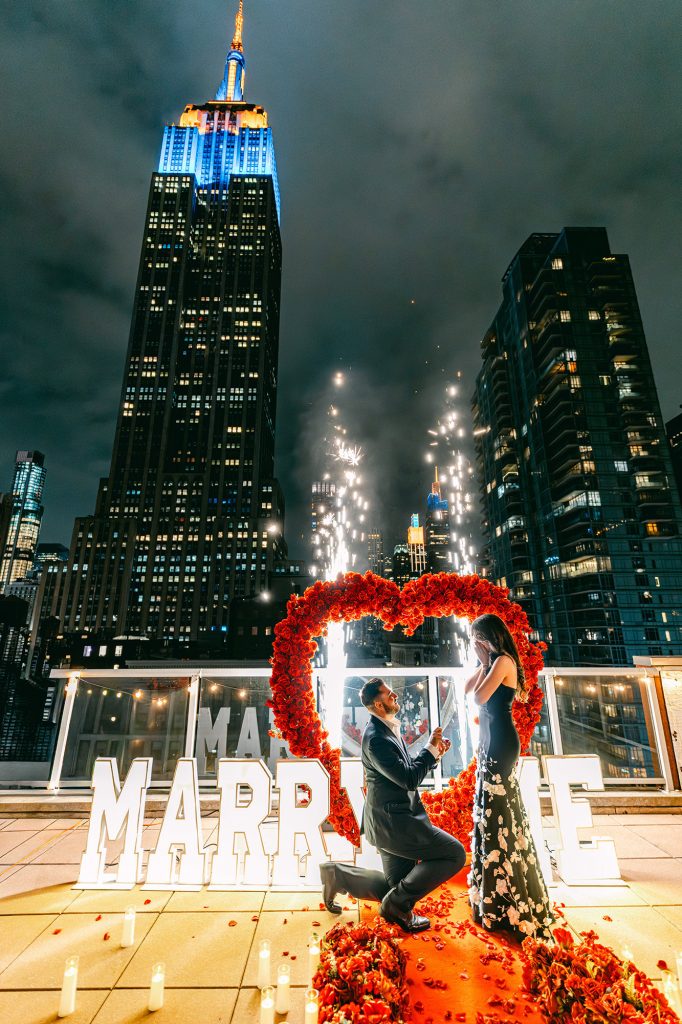 Proposal at Empire State View Rooftop in Manhattan, inside a red rose heart with the Empire State Building lit behind