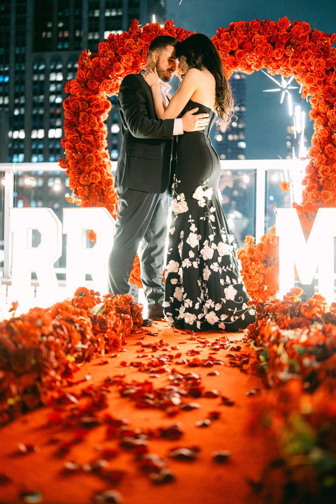 Newly engaged couple inside a red rose heart at Empire State View Rooftop, Manhattan, at night