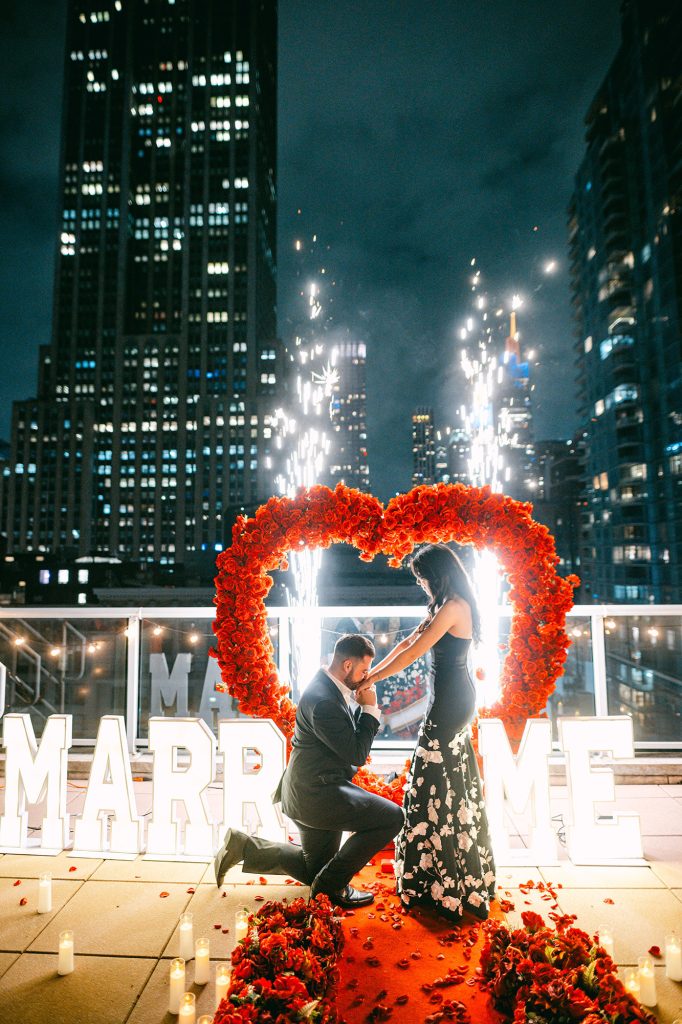 Man on one knee inside a red rose heart at Empire State View Rooftop with sparklers and MARRY ME letters