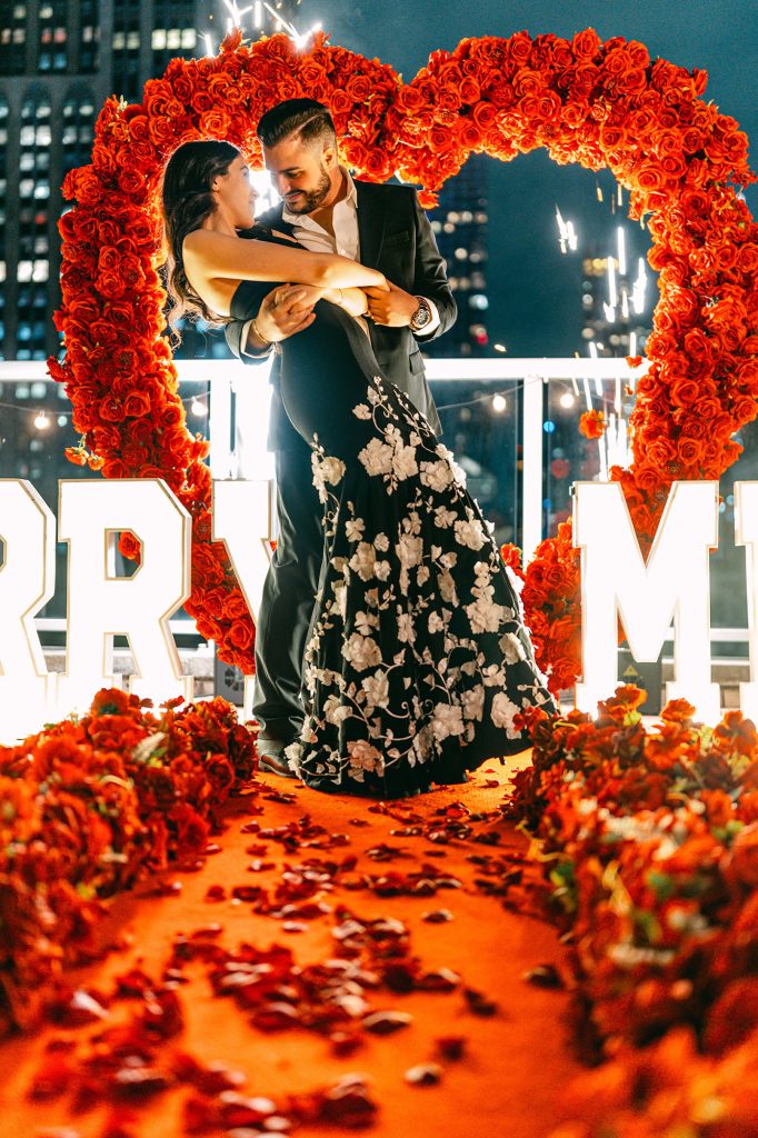 Couple dipping inside a red rose heart arch at Empire State View Rooftop, Manhattan, at night