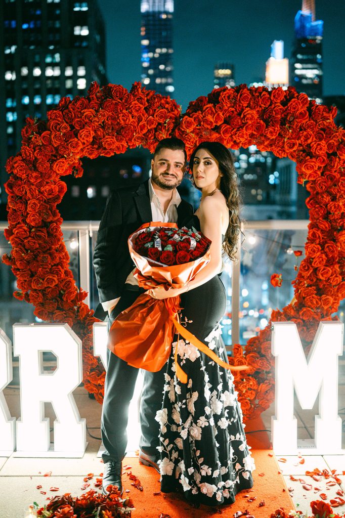 Newly engaged couple with red roses inside a rose heart at Empire State View Rooftop, Manhattan