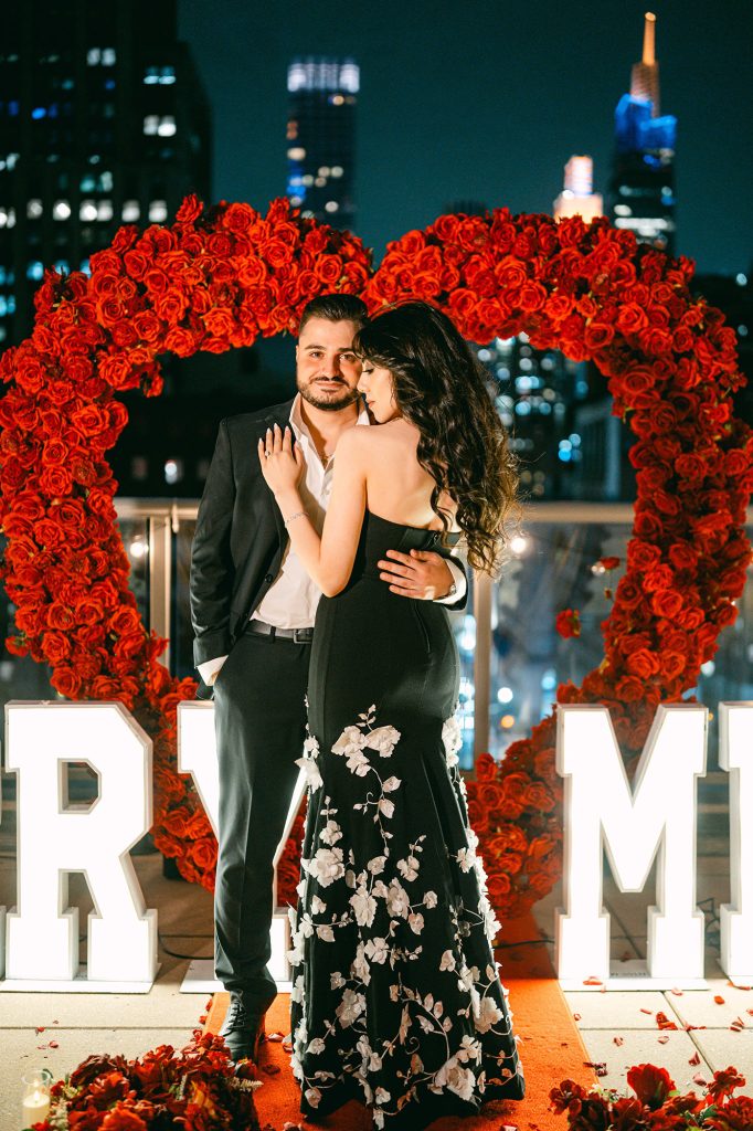 Couple embracing inside a red rose heart arch at Empire State View Rooftop in New York City