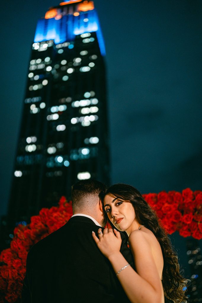 Close engagement portrait with red roses out of focus at Empire State View Rooftop, Manhattan