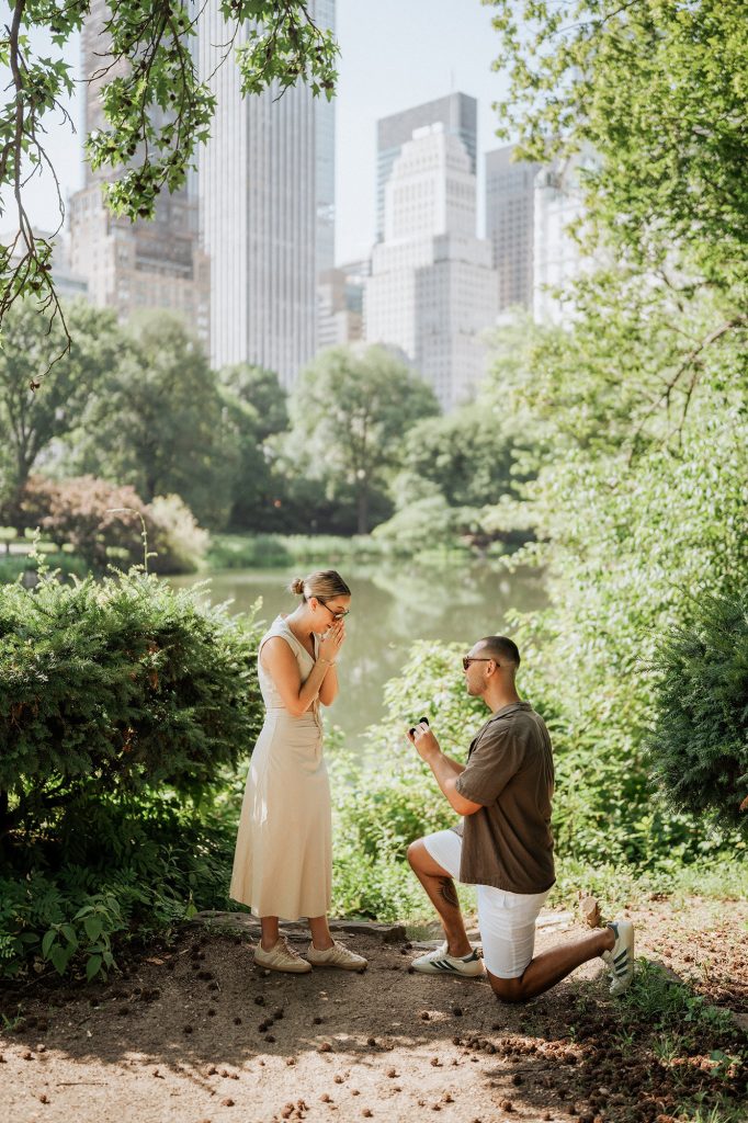 Surprise proposal by the Lake in Central Park with the Midtown skyline behind the trees
