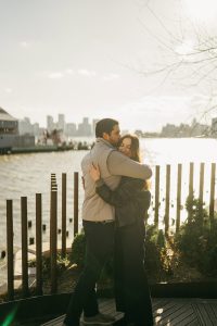 Newly engaged couple embracing at Little Island in Manhattan, the Hudson River behind them