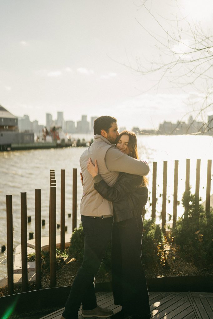 Newly engaged couple embracing at Little Island in Manhattan, the Hudson River behind them