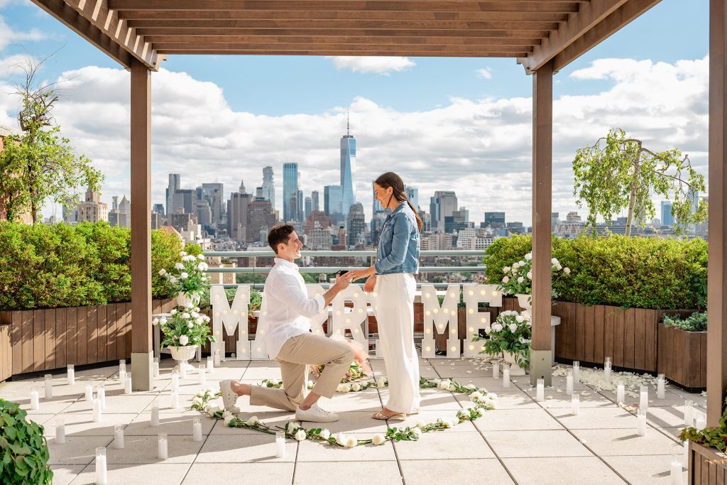 Proposal on a private Manhattan rooftop under a pergola with MARRY ME letters and a white flower heart