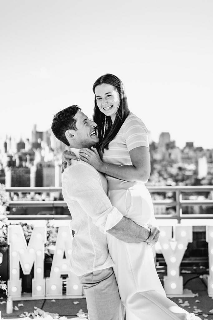 Black and white photograph of a newly engaged couple laughing on a private Manhattan rooftop