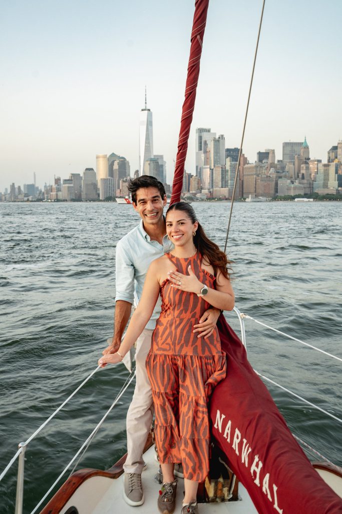 Newly engaged couple at the bow of a yacht in New York with One World Trade Center behind