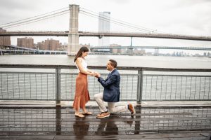 Proposal at Pier 17: man on one knee, the Brooklyn and Manhattan bridges behind them