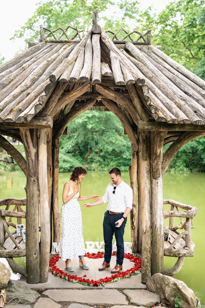 Couple standing inside a rose petal heart under the rustic wooden shelter at Wagner Cove, Central Park