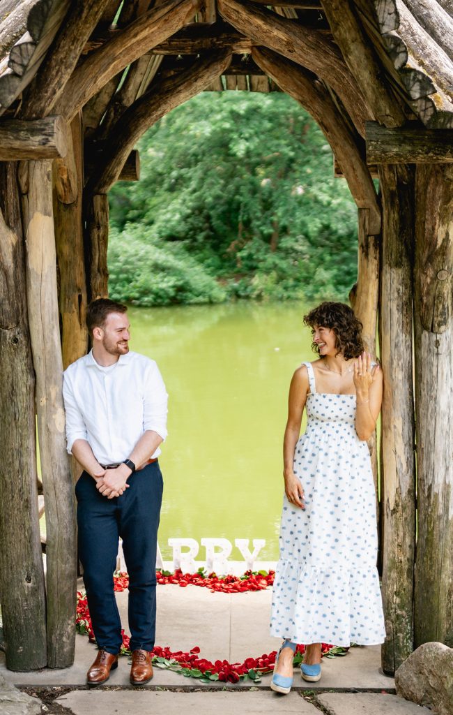 Couple standing on either side of a rose petal heart with MARRY ME letters at Wagner Cove, Central Park